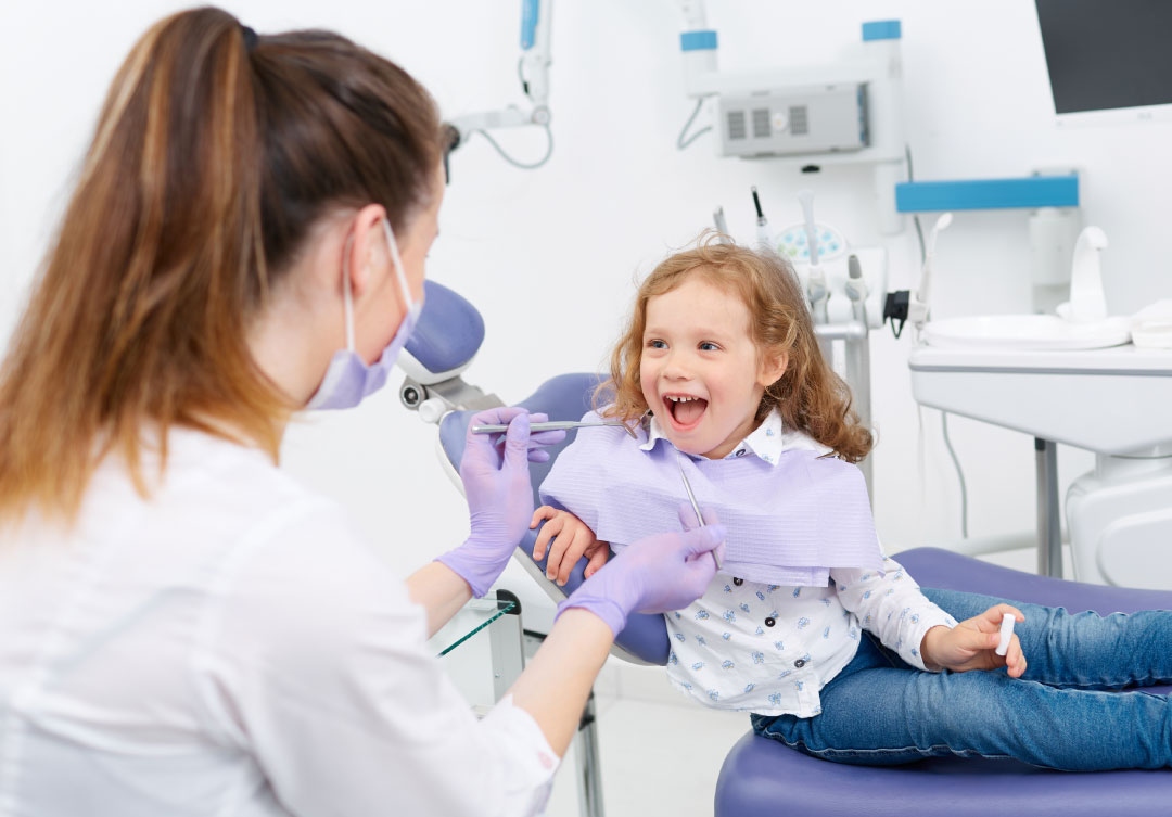 A pediatric dentist is checking on a happy little girl in a pediatric dentistry office.