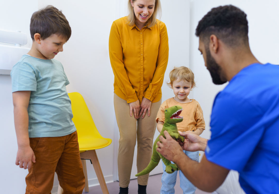A friendly pediatric dentist is showing two kids a toy to make them feel comfortable.